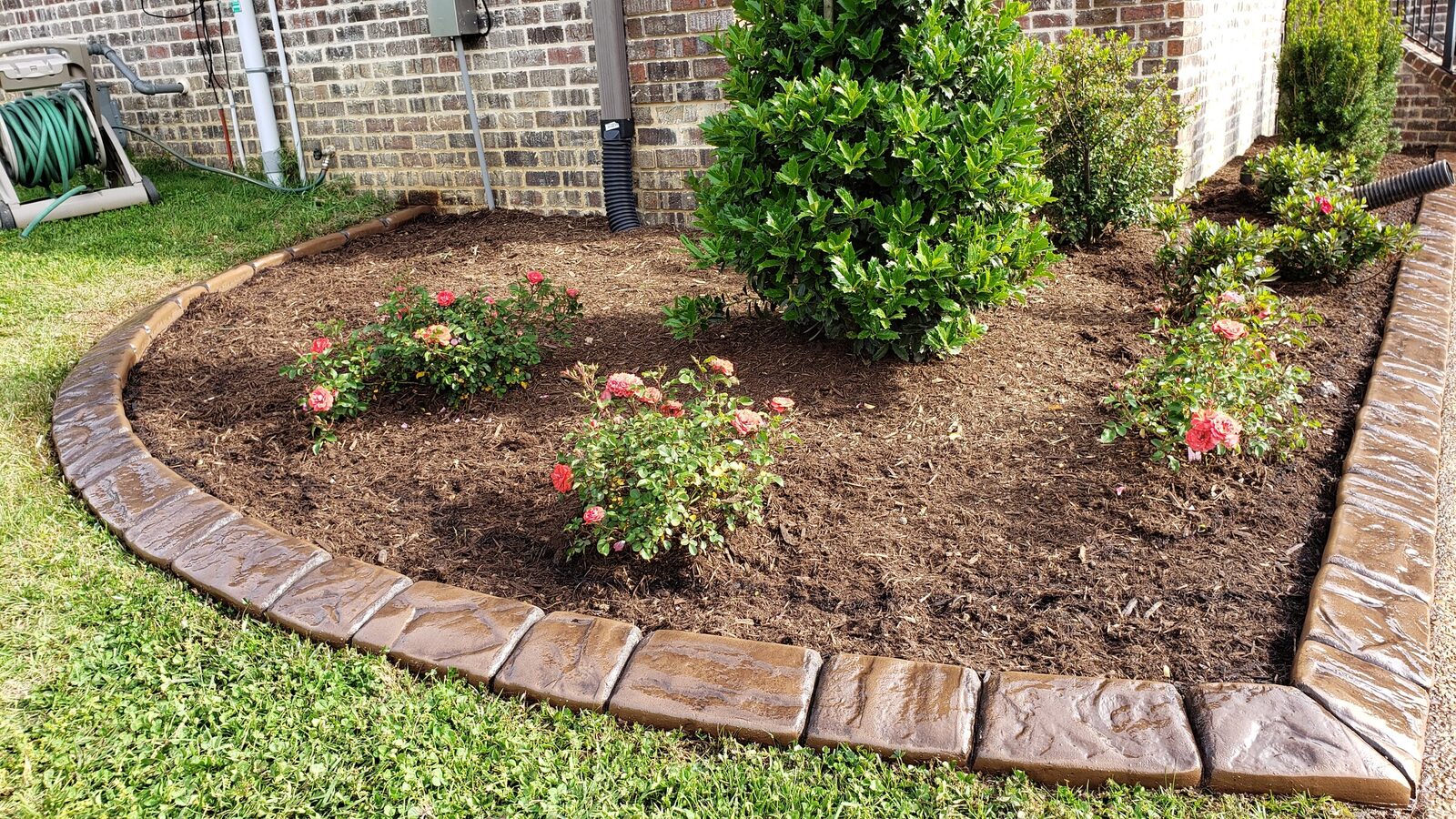Brown stamped curbing around a rose bed beside a brick home