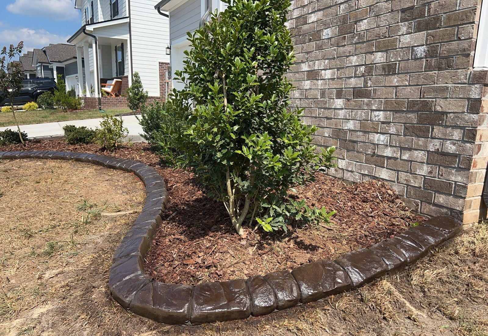 Chattanooga Rock curbing curving around a holly bed at a brick corner