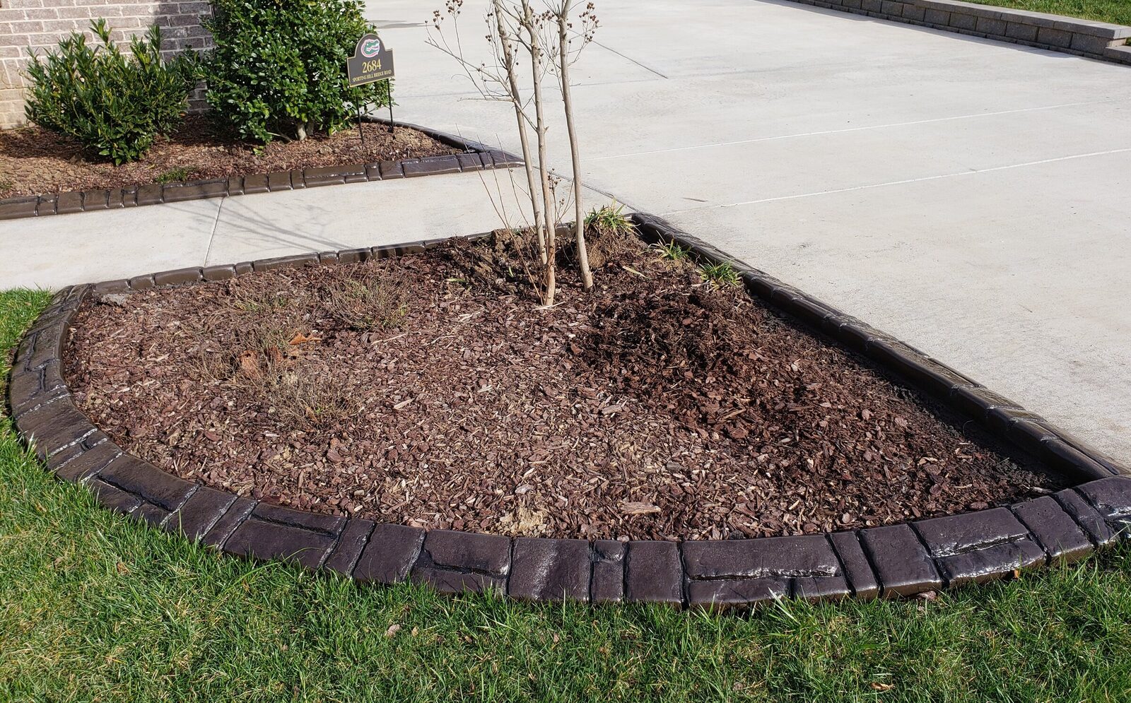 Dark brown stamped curbing around a tree bed beside a driveway