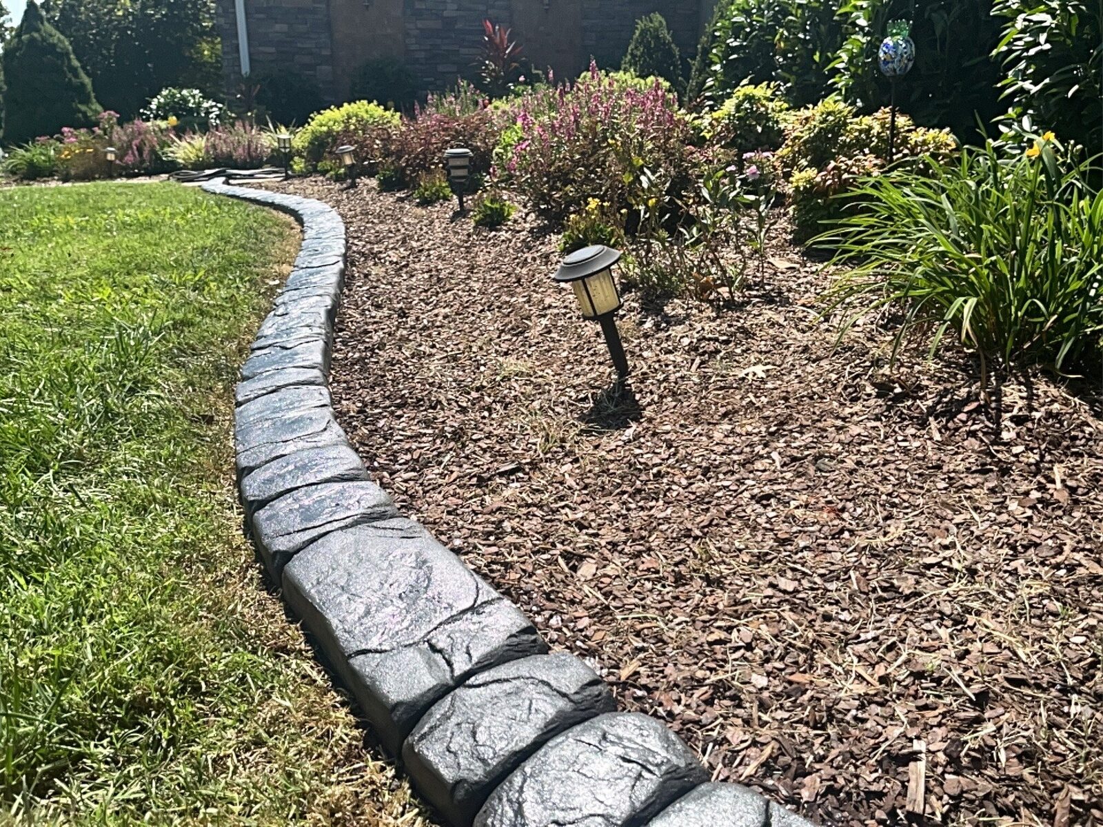 Grey stamped curbing edging a mulch bed with a solar path light