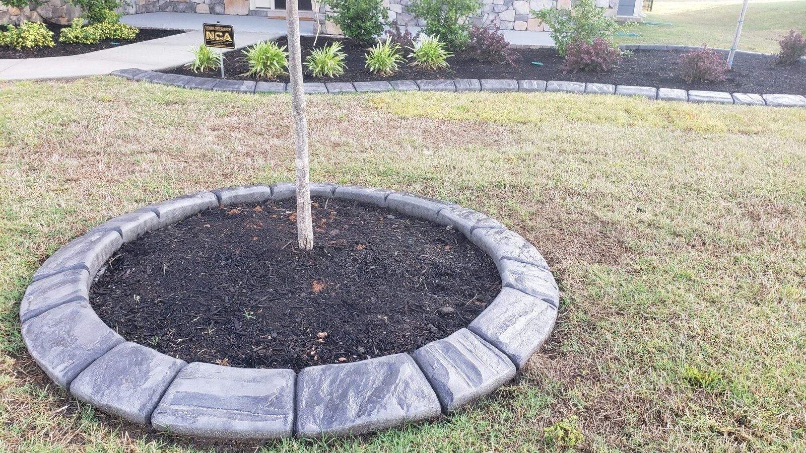 Continuous grey stamped curb forming a tree ring in a front lawn