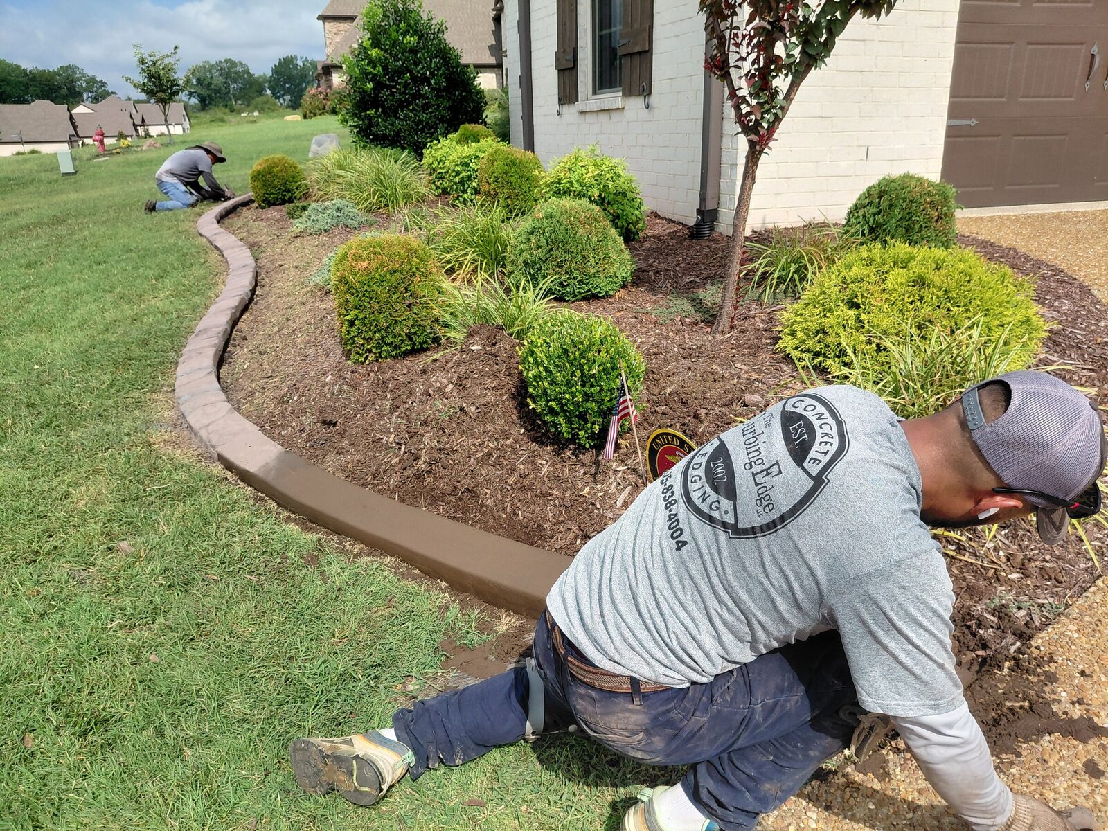 A crew member hand-finishing a fresh curb along a foundation bed