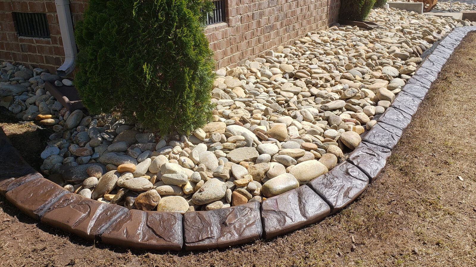 Curb holding river rock in a foundation bed