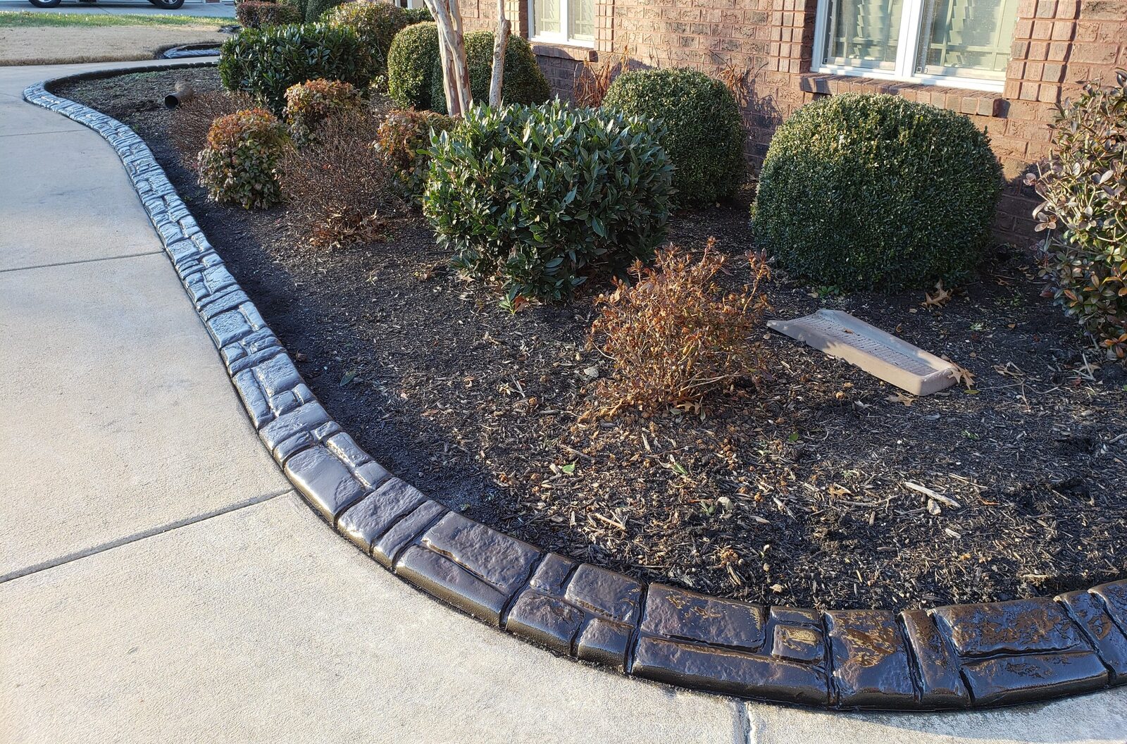 Finished stamped curbing along a boxwood foundation bed at a brick home